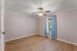 Light-filled room featuring wood-finish flooring, a ceiling fan with integrated lighting, and crown molding