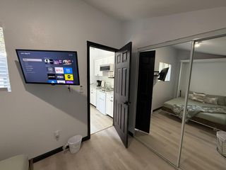 Furnished bedroom with a wall-mounted TV, mirrored closet doors, and easy access to the adjacent kitchenette.