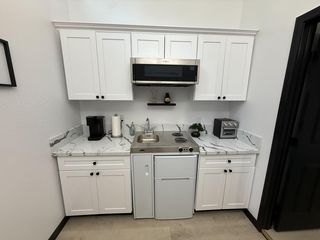 Streamlined kitchenette with shaker cabinetry, marble-look counters, stainless sink, and microwave over a 2-burner cooktop.